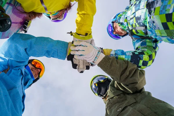 Foto abajo de cuatro snowboarders con casco y máscara haciendo apretón de manos —  Fotos de Stock