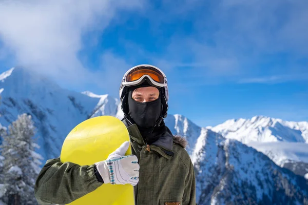 Fotografie sportovce v helmě a brýlích se žlutým snowboardem v lyžařském středisku . — Stock fotografie