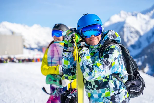 Αθλητής και γυναίκα snowboarders στέκεται στο χιονοδρομικό κέντρο με φόντο το βουνό. — Φωτογραφία Αρχείου