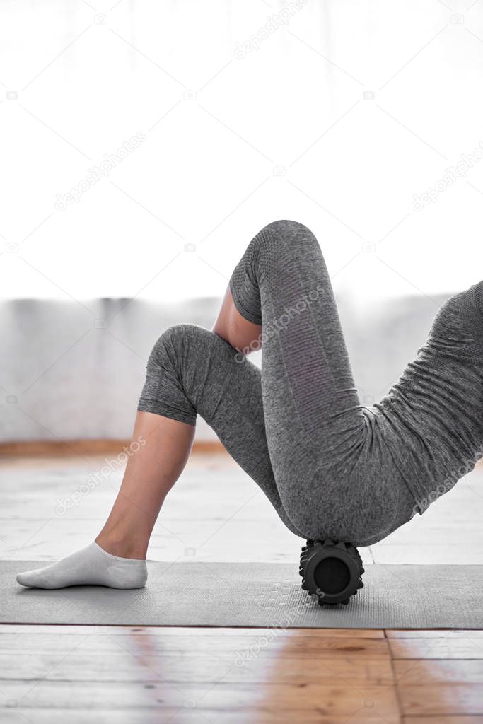 Young woman doing yoga lying on massager on mat on wooden floor in gym