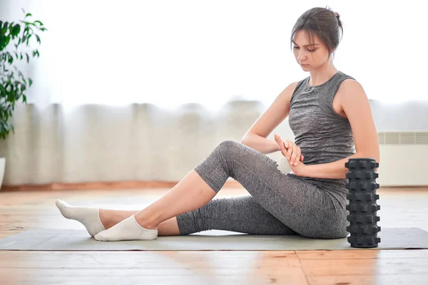 Sportowa brunetka na treningu z masażerem siedzącym na dywanie — Zdjęcie stockowe