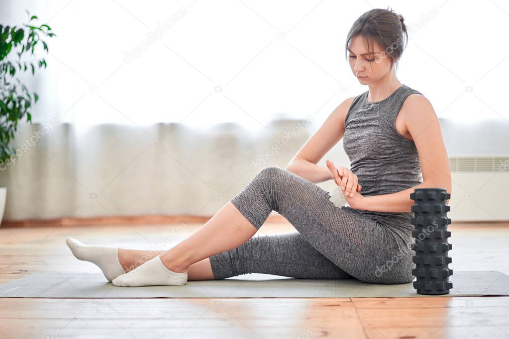 Athletic brunette in training with massager sitting on rug