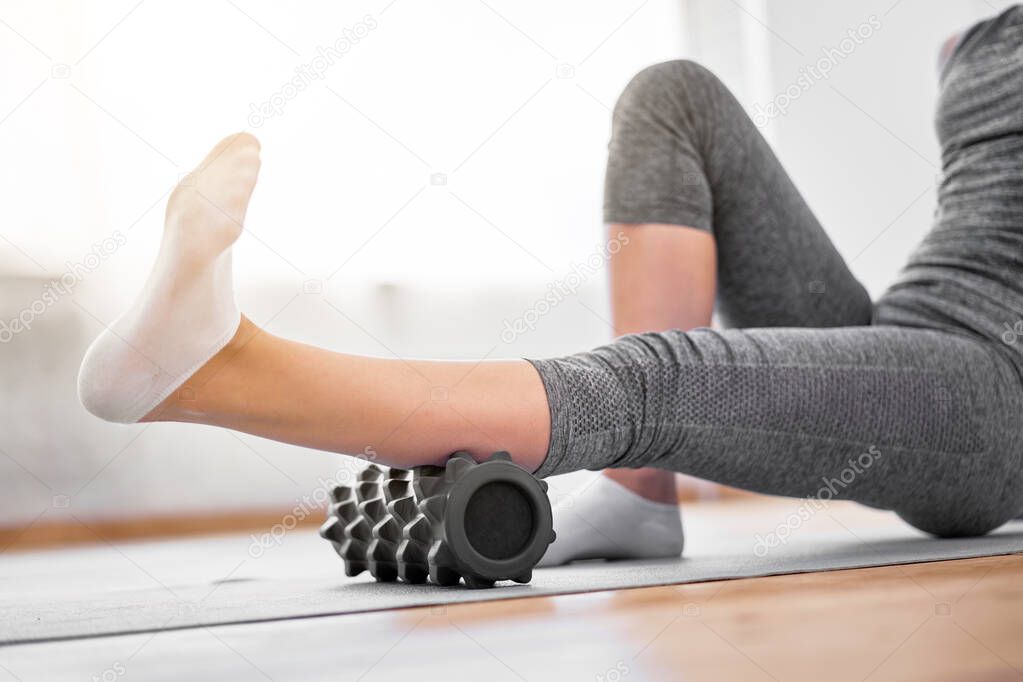 Young girl doing yoga while lying on massager on rug on wooden floor against background of window in gym