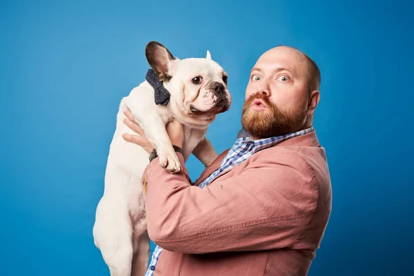 Mâle chauve vêtu d'un bouledogue français dans les bras sur fond bleu vide — Photo