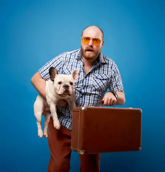 Szakállas férfi bulldog és poggyász üres kék háttér — Stock Fotó