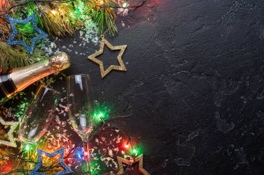 Köknar dalları, Noel süslemeleri mavi ve altın oyuncaklar, yanan çelenkler, şampanya şişeleri, siyah arka planda iki şarap kadehi