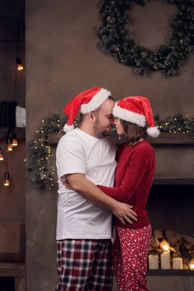 Foto lateral de abrazar a hombres y mujeres en gorra de Santas en la habitación —  Fotos de Stock