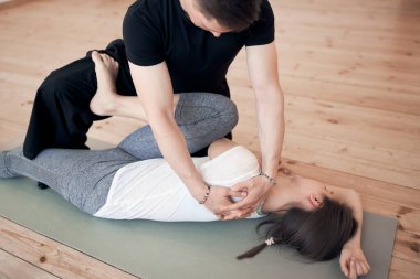 Beyaz tişörtlü kadın için egzersiz yapan bir adam spor salonunda gri halıda yatıyor.