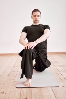 Genç adam spor salonunda gri halıda otururken meditasyon yapıyor.