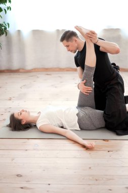 Young woman doing stretching on mat with male trainer in black suit in gym clipart