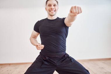 Siyah eşofmanlı genç esmer, salonda dövüş sanatlarıyla meşgul.