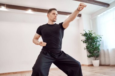 Genç adam yeşil bitkinin arka planında karate yapıyor.