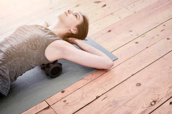 Donna che fa yoga sdraiato sul massaggiatore sul tappeto sul pavimento in legno in palestra — Foto Stock