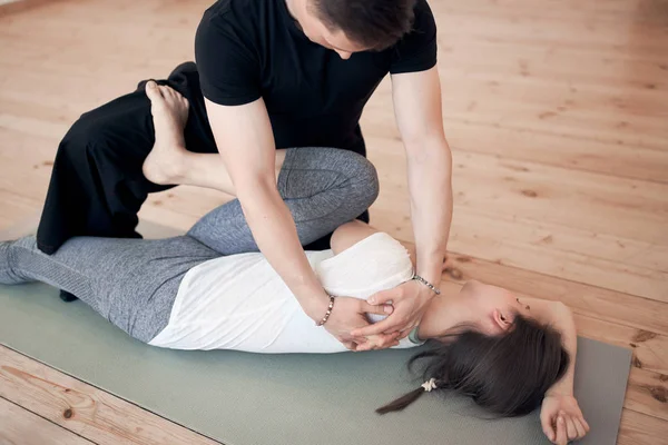 Man doing stretching exercises for woman in white T-shirt lying on gray rug in gym — Stock Photo, Image