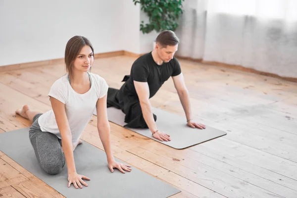 Man and brunette woman doing yoga sitting on gray rug in room during day — Stock Photo, Image