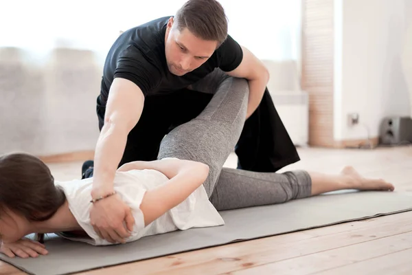 Brunette girl doing stretching on mat with male trainer — Stock Photo, Image