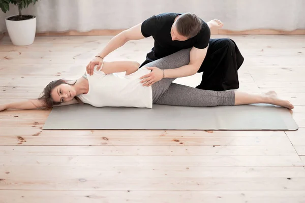 Brunette woman doing stretching on grey mat with male trainer — Stock Photo, Image