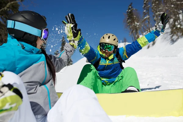Donna che fa stretta di mano con uomo felice con snowboard seduto sul fianco della collina . — Foto Stock