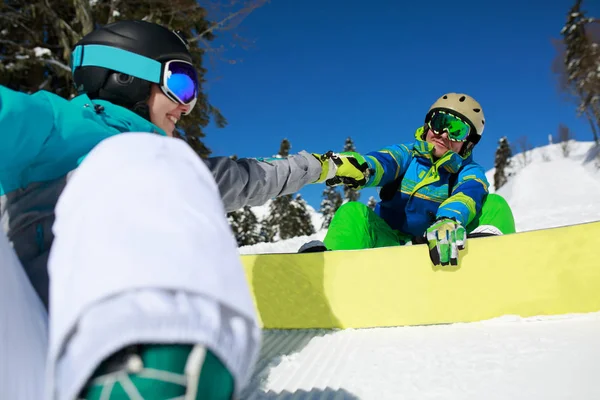 Femme masquée faisant poignée de main avec l'homme heureux avec snowboard assis sur la colline . — Photo