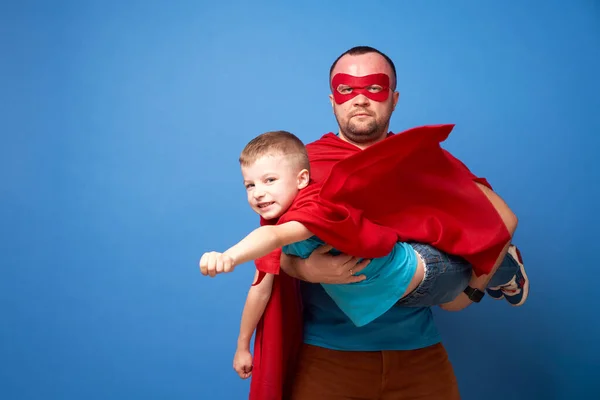 Mann mit Maske und fliegender Sohn Superhelden in roten Mänteln auf blauem Hintergrund — Stockfoto