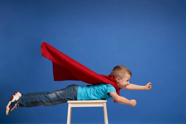 Junge in rotem Superheldenmantel fliegt auf leeren blauen Hintergrund — Stockfoto