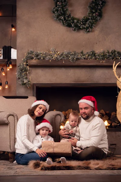 Foto van ouders in Santas pet met twee zoons zittend op de vloer bij open haard in de kamer — Stockfoto