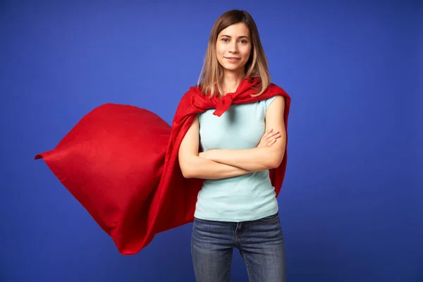 Kvinna i röd superhjälte mantel står på tom blå bakgrund — Stockfoto