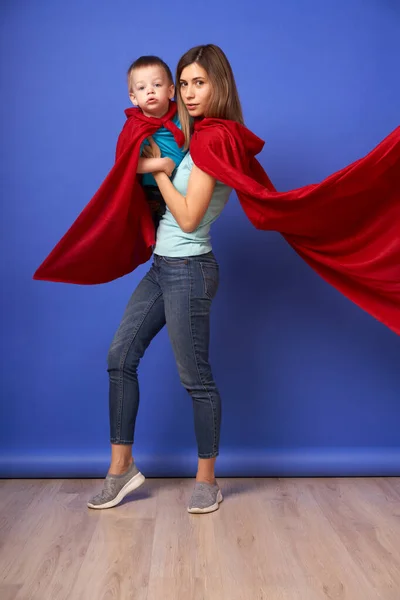 妈妈和儿子的超级英雄穿着红色的衣服，背景是空旷的蓝色 — 图库照片