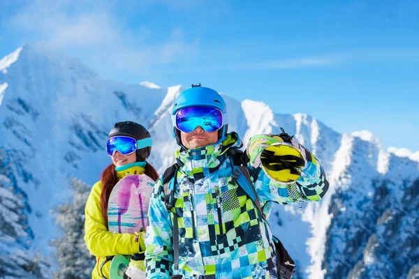 Happy man and brunette woman snowboarders standing on snow resort against backdrop of mountain in afternoon. — Stock Photo, Image