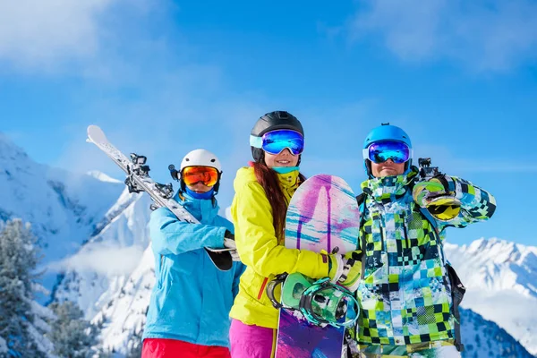 Sportsmen et femme avec snowboard et skis debout sur la station de neige sur fond de montagne et ciel nuageux — Photo