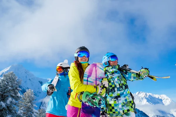Men and woman with snowboard and skis looking in different directions standing on snow resort against background of mountain and cloudy sky. — Stock Photo, Image