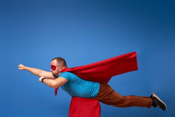 Man i röd superhjälte mantel flyger på tom blå bakgrund — Stockfoto