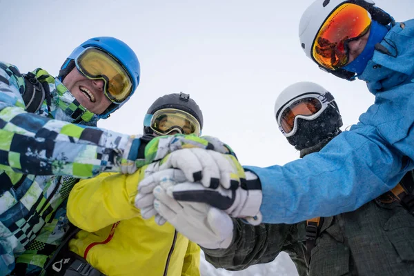 Imagen de la parte inferior de cuatro snowboarders felices en casco haciendo apretón de manos —  Fotos de Stock