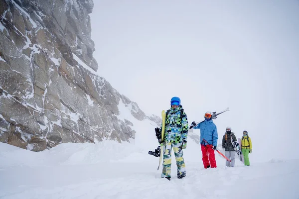 Imagen de cuatro deportistas con esquís y snowboard caminando en estación invernal —  Fotos de Stock