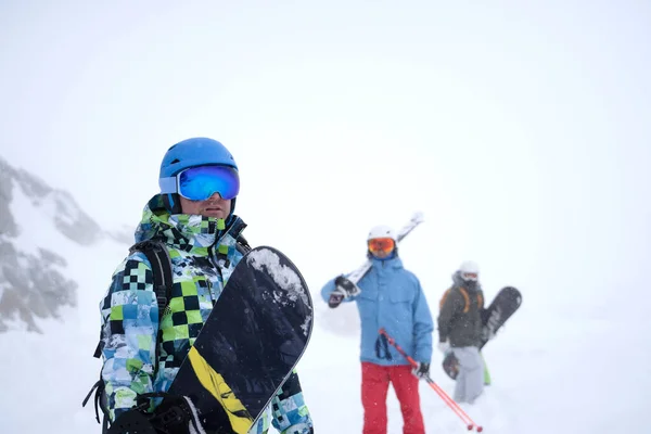 Foto di tre sportivi con sci e snowboard che camminano attraverso la località invernale — Foto Stock