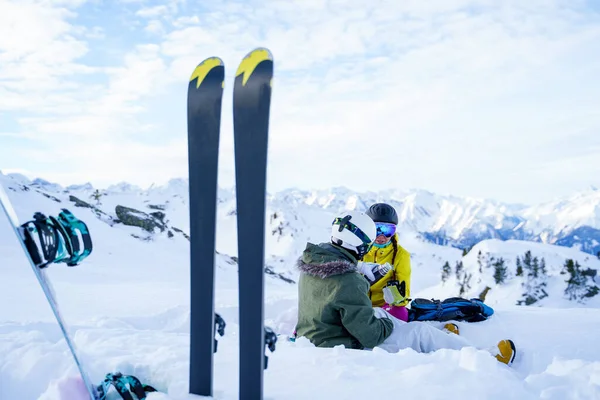 Zdjęcie nart, kijków narciarskich na tle dwóch sportowców z termosem siedzących zimą w ośrodku narciarskim. — Zdjęcie stockowe