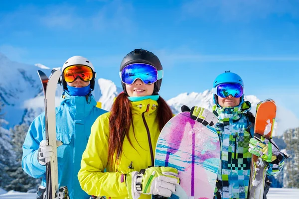 Desportistas e mulher com snowboard e esquis em pé no resort de neve contra o pano de fundo da montanha . — Fotografia de Stock