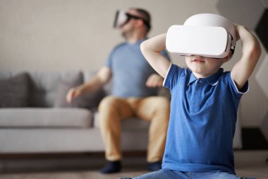 Genç baba ve oğul dairede sanal gerçeklik gözlüğü takıyor.