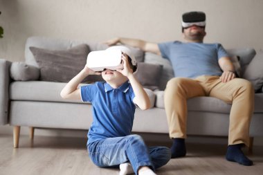 Genç bir adam ve küçük bir çocuk dairede sanal gerçeklik gözlüğü takıyorlar.