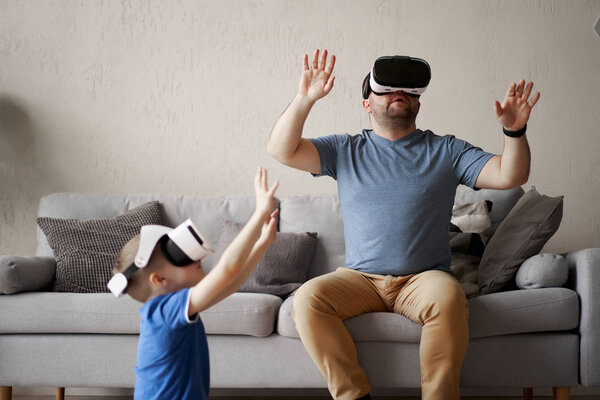 Man and small son in glasses of virtual reality in apartment