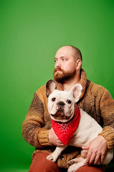 Egy szakállas férfi, aki francia bulldoggal a karjában áll. — Stock Fotó