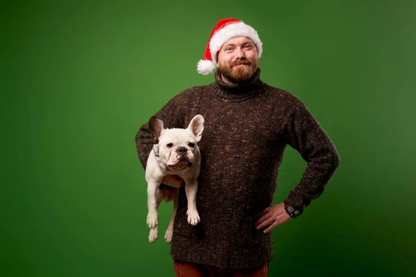 Smiling man in santa hat with bulldog on empty green background — Stock Photo, Image