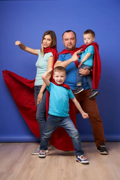 Young parents and children superheroes in red cloaks on blank blue background — Stock Photo, Image