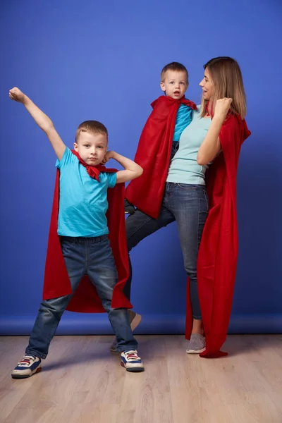 Mamma e due figli supereroi in mantelli rossi su sfondo blu vuoto — Foto Stock