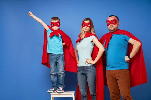 Anya és apa, gyerekek szuperhősök piros köpenyben üres kék háttér — Stock Fotó