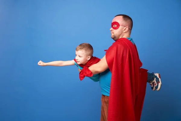 Papa und fliegender Sohn Superhelden in roten Mänteln auf blauem Hintergrund — Stockfoto