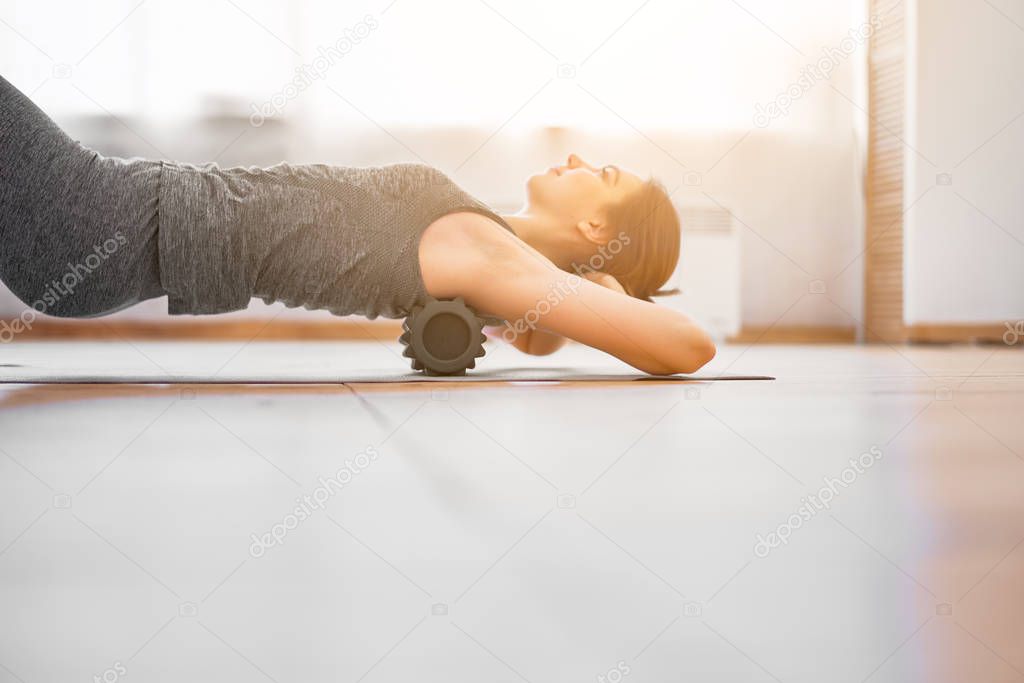 Girl doing yoga lying on massager on rug in gym during day.
