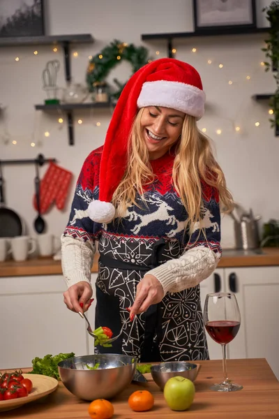 Ευτυχισμένο κορίτσι στο καπέλο santa μαγειρεύει ενώ στέκεται στην κουζίνα. — Φωτογραφία Αρχείου