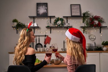 Noel 'de mutfakta şarap kadehleriyle şenlik masasında oturan iki kıvırcık kız..