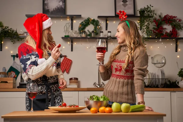 Δύο νεαρές γυναίκες με ποτήρια κρασιού για την Πρωτοχρονιά στην κουζίνα — Φωτογραφία Αρχείου